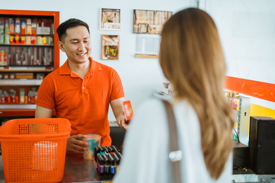 male shopkeeper serves female shoppers by scanning barcodes at the checkout at the minimarket