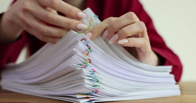 Woman organizes stack of paper documents with colorful paper clips
