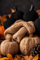 Hand-knit pumpkins in black and brown, wrapped in cozy knitted fabric, surrounded by pinecones and autumn leaves, creating a warm and rustic seasonal scene