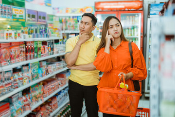 husband and wife upset when shopping carrying a red shopping cart in the supermarket