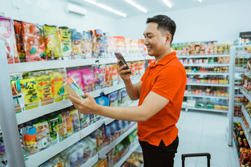 Asian male shop worker stands photographing an item at a minimarket