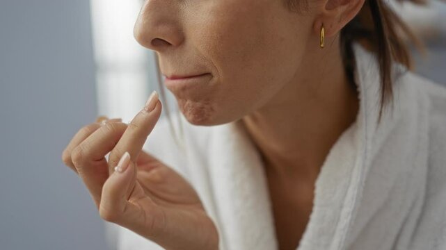 Woman applying lip balm in spa room while wearing a white robe, showcasing beauty and self-care