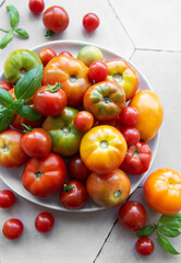 Fresh assorted  tomatoes arranged on a white plate with green basil leaves in a bright kitchen setting