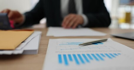 Male office worker stamps on documents sitting at workplace with analytics papers. Manager in official suit works hardly preparing documentation for investors