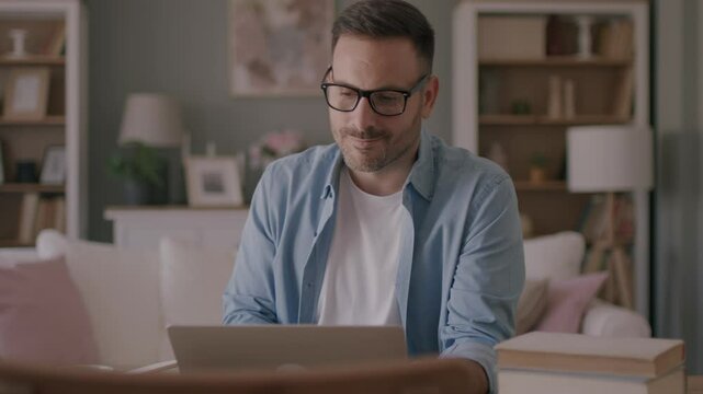 A focused mid aged male freelancer sitting at the wooden table at home and reading online projects on a laptop. 4k video