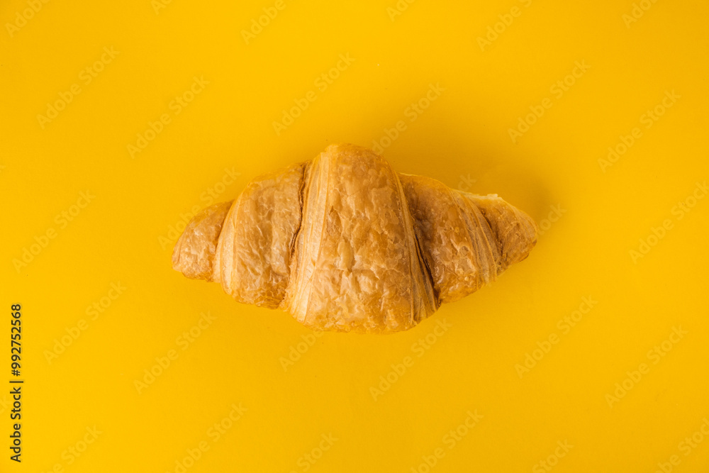 Wall mural flat lay of single freshly baked croissant on the yellow background. traditional french pastry with 