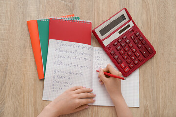 Woman writing math formulas in copybook on wooden table