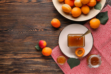 Glass bowl and jars with sweet apricot jam on wooden background
