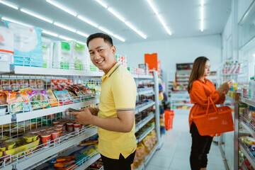 handsome man smiles into the camera while standing in front of a shelf in a supermarket