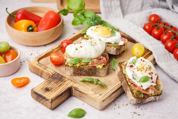 Wooden board of tasty sandwiches with egg on light background
