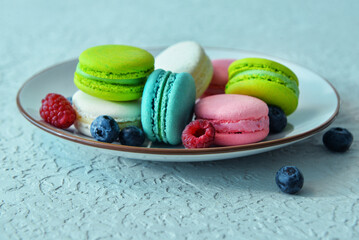 Plate with sweet macaroons and berries on light blue background