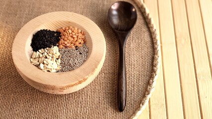 Wooden bowl holding chia seeds, oats, black sesame, lentils paired with wooden spoon on woven mat. Simple, eco-friendly arrangement showcasing sustainable, plant-based nutrition choices Wooden tools