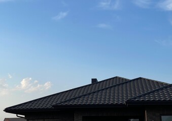 Three-slope black roof on the background of the sky. Complex slopes of the roof. Use of metal tiles