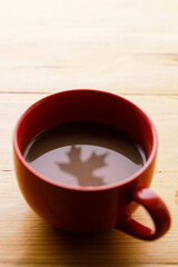 Cup of delicious hot chocolate with red maple leaf reflection on wooden table background. Selective focus.