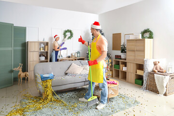 Young janitors in Santa hats cleaning room after New Year party