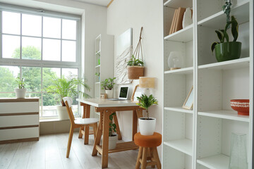 Interior of light living room with green houseplants, workplace and shelf units