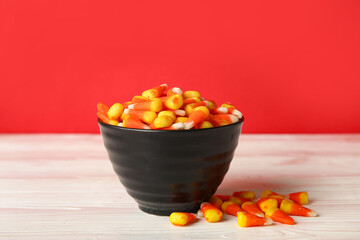 Bowl of Halloween candies on wooden table against red background