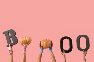 Hands of zombies with word BOO and ripe pumpkins on pink background. Halloween celebration