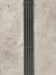 Rectangular metal drain grate set into a dry earth. There is a slight lip around the edge of the...