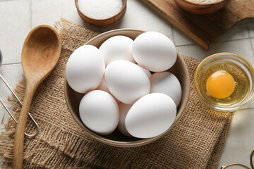 Bowl with raw chicken eggs and sugar on white tile background