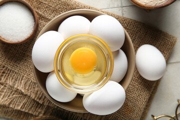 Bowl with raw chicken eggs and sugar on white tile background