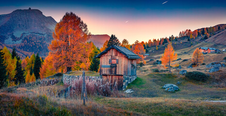 Panoramic autumn view of wooden chalet in Fuchiade valley. Great sunset in  Dolomite Alps, Italy, Europe. Beauty of countryside concept background.