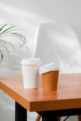 A disposable coffee cup on a wooden table beside a leafy plant
