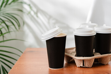 Takeout coffee cups placed on a wooden table next to a green indoor plant