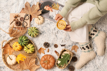 Female legs in warm socks with autumn leaves, pumpkins and cup of tea on white plaid as background