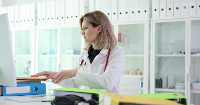 Female medic inserts paper documents into folder for patient data storage. Concept of sorting and workflow of specialist at workplace. Medical profession
