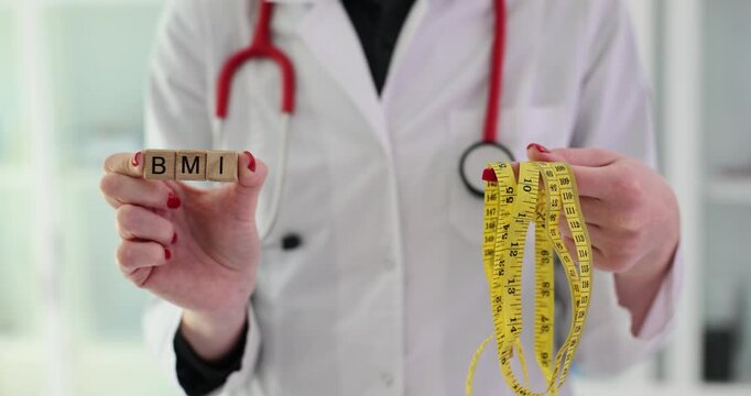 Doctor holds word BMI from wooden blocks and measuring tape to measure standing in clinic office. Body mass index and device for measuring parameters