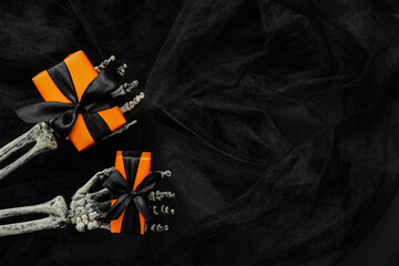 Halloween gifts, skeleton hands and tulle on black background. Top view