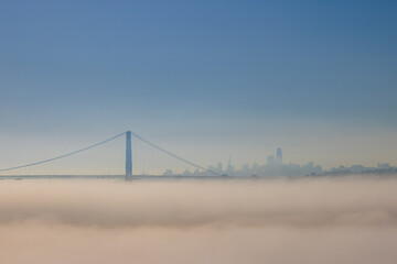 Golden Gate Bridge above fog with city skyline in distance on sunny day