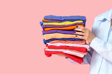 Young woman with stack of colorful clothes on pink background, closeup