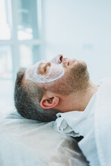 Obraz premium A man with a mask in a beauty salon. Men's face care concept. A beautician puts a mask on a client's face in a spa center. Male cosmetology.