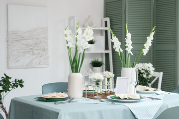 Table setting with white Gladiolus flowers and burning candles in room