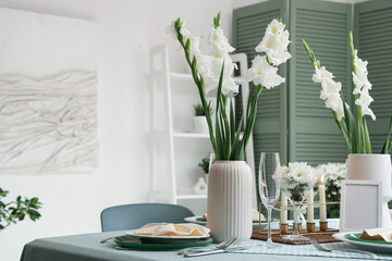 Table setting with white Gladiolus flowers and burning candles in room