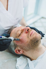 Obraz premium A beautician makes a mask on the face of a man with a beard. Male cosmetology. Preservation of youth and facial skin care. Beauty salon concept.