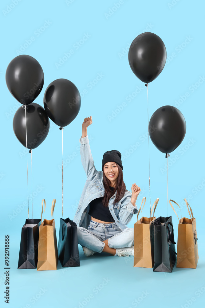 Sticker Young Asian woman with shopping bags and balloons sitting on blue background. Black Friday Sale