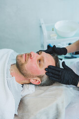 Obraz premium A cosmetologist cleans the skin of a man's face. A man does facial procedures in a cosmetic clinic. Male cosmetology.