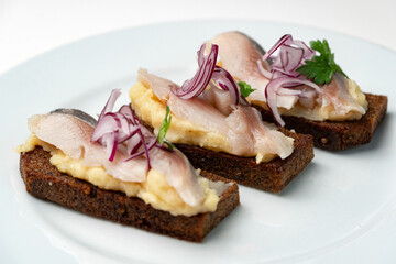 Open-faced sandwiches with herring and onions served on a white plate