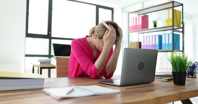 Young woman doomed grabs head holding bank card in hand against laptop. Lady in office realizes being deceived on Internet. Internet fraud concept
