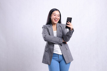 Naklejka premium Beautiful adult office woman cheerful to mobile phone and holding cellphone wearing gray suit isolated on white background. for technology, lifestyle, shopping, transaction content
