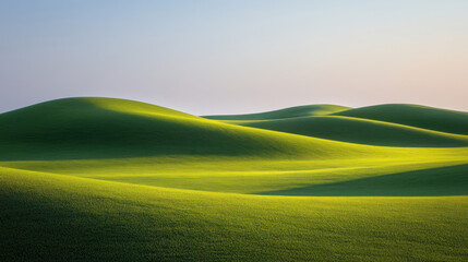 Gently lit green hills with smooth curves under a clear sky, representing peaceful natural beauty and tranquility.