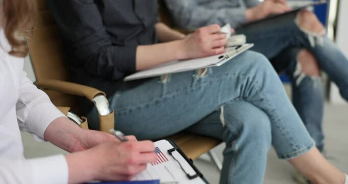 Applicants for getting American Visa sit in queue in embassy office filling in blanks for personal information holding passports with money. Preparation for interview