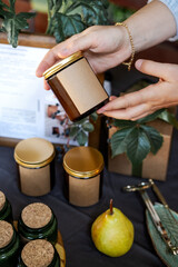 Handmade candle in the glass. Female hands is holding it, blank space for text on the label. Rustic, autumn, cosy vibes.