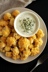 Homemade Buffalo Cauliflower with Blue Cheese Sauce on a Plate on a Black Background, top view.