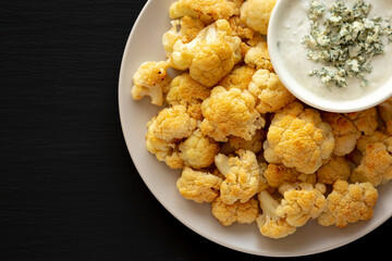 Homemade Buffalo Cauliflower with Blue Cheese Sauce on a Plate on a Black Background, top view. Copy space.