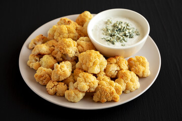 Homemade Buffalo Cauliflower with Blue Cheese Sauce on a Plate on a Black Background, side view.