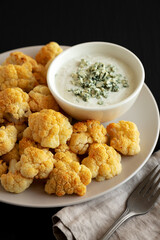 Homemade Buffalo Cauliflower with Blue Cheese Sauce on a Plate on a Black Background, side view.